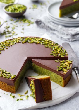 Flourless Pistachio Cake with Chocolate Ganache on a gray background, two slices cut to show the bright green color inside.