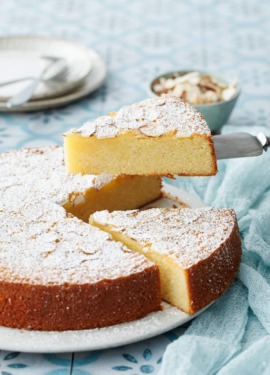 Slice of Flourless Almond Flour Cake lifted by a cake knife, on a blue tile background with linen napkin.
