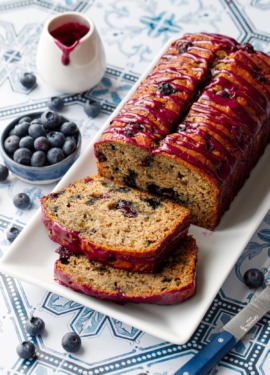 Loaf of Blueberry Banana Bread on a white rectangular plate with two slices lying down on a blue and white tile background.
