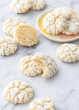 Chewy Lemon Almond Crinkle Cookies scattered on a marble background with a few cookies on a small cookie plate.