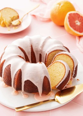 Grapefruit Olive Oil Bundt Cake with two cut slices leaning against each other, on a white cake plate and cut grapefruit and a slice of cake in the background.